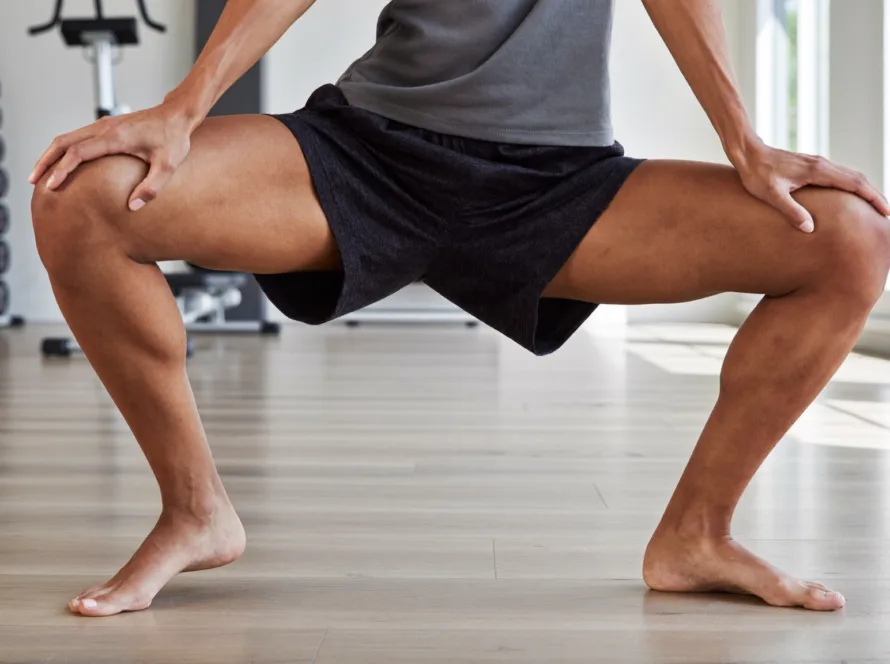 Persona realizando un ejercicio de movilidad articular de cadera en sentadilla profunda en un gimnasio luminoso
