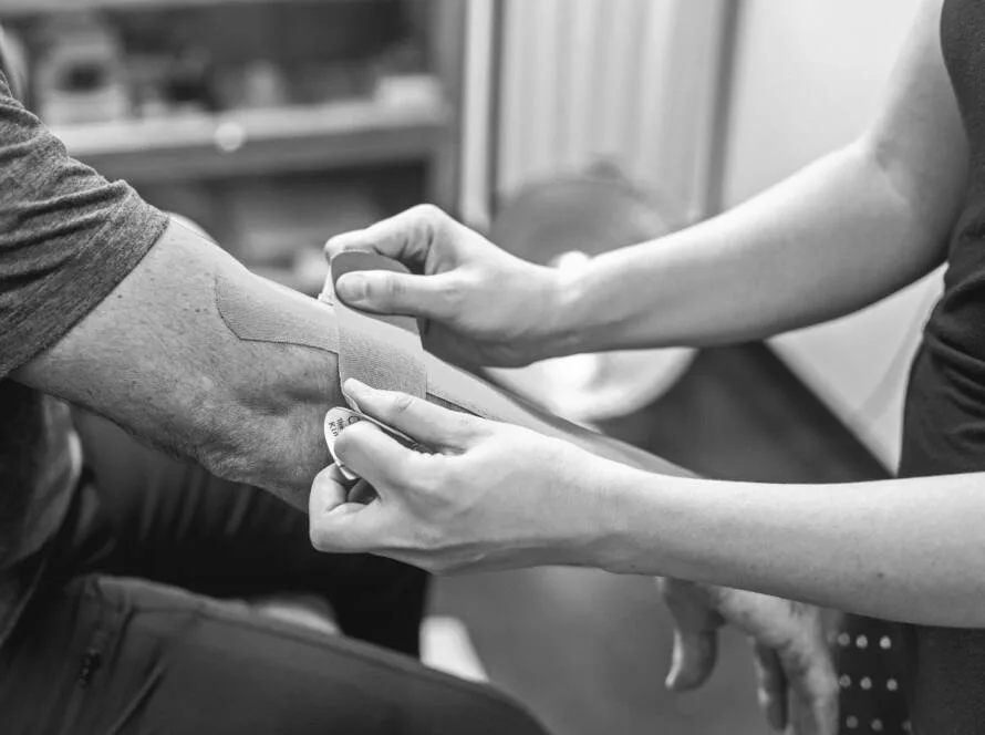 Fisioterapeuta aplicando vendaje neuromuscular en el codo de un paciente para tratar el codo de tenista o epicondilitis lateral