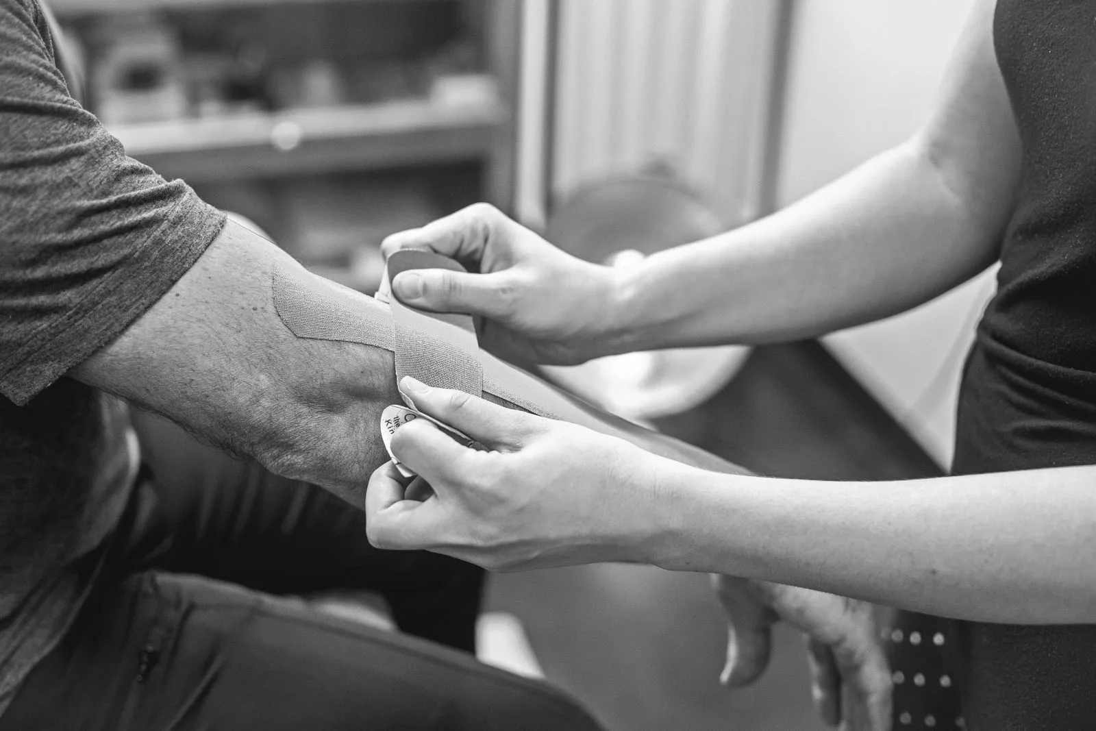 Fisioterapeuta aplicando vendaje neuromuscular en el codo de un paciente para tratar el codo de tenista o epicondilitis lateral